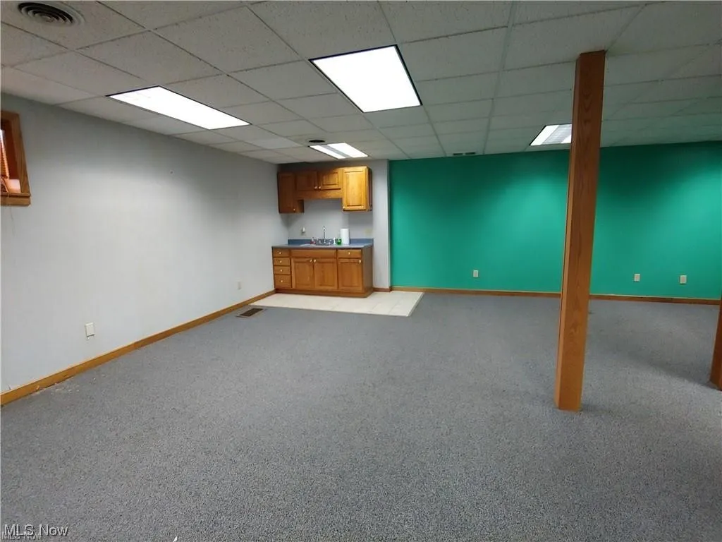 Basement with light colored carpet, indoor wet bar, and a drop ceiling