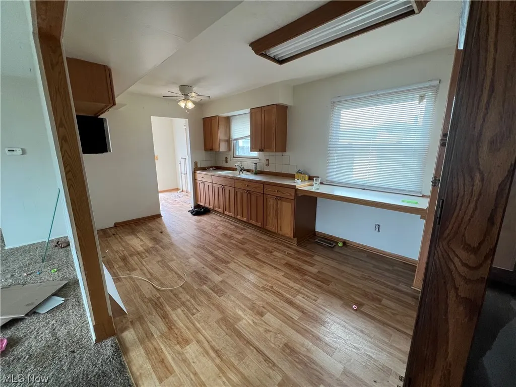 Kitchen with ceiling fan, light wood-type flooring, sink, and backsplash