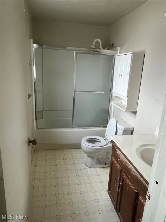 Full bathroom with toilet, tile flooring, combined bath / shower with glass door, and vanity