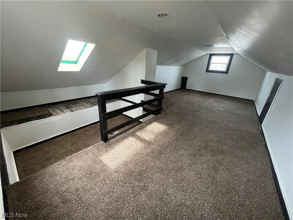 Bonus room with lofted ceiling with skylight and dark colored carpet