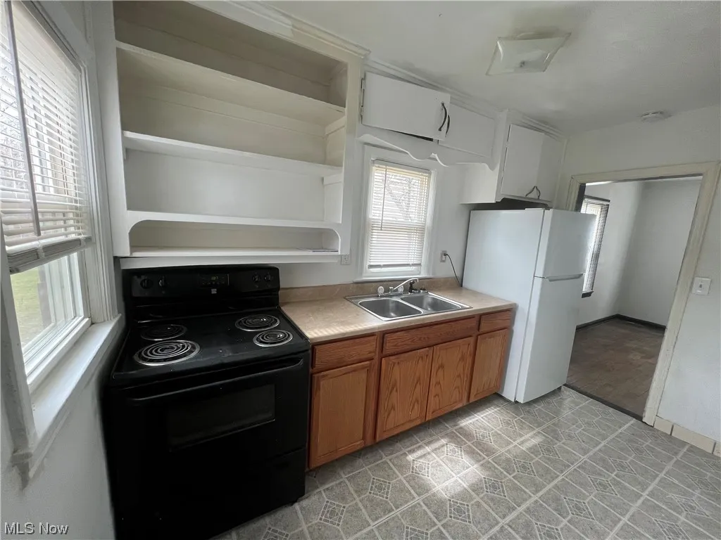 Kitchen featuring light tile floors, sink, black / electric stove, and white fridge