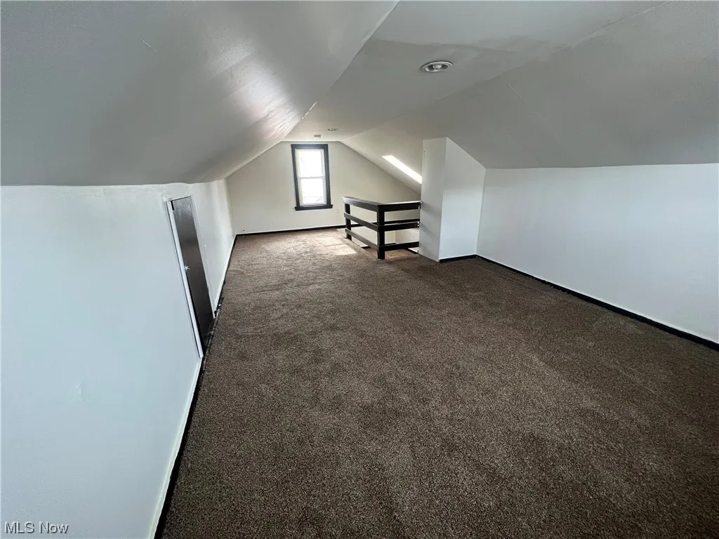 Bonus room featuring dark colored carpet and vaulted ceiling