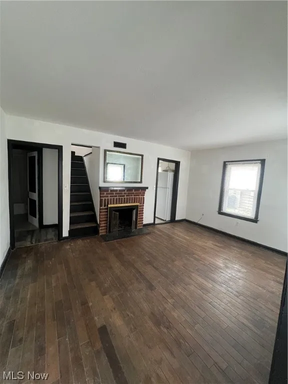 Unfurnished living room featuring dark hardwood / wood-style flooring and a brick​​‌​​​​‌​​‌‌​‌‌​​​‌‌​‌​‌​‌​​​‌​​ fireplace