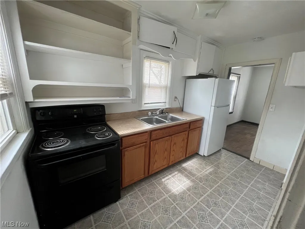 Kitchen with white refrigerator, sink, light tile flooring, and black electric range oven