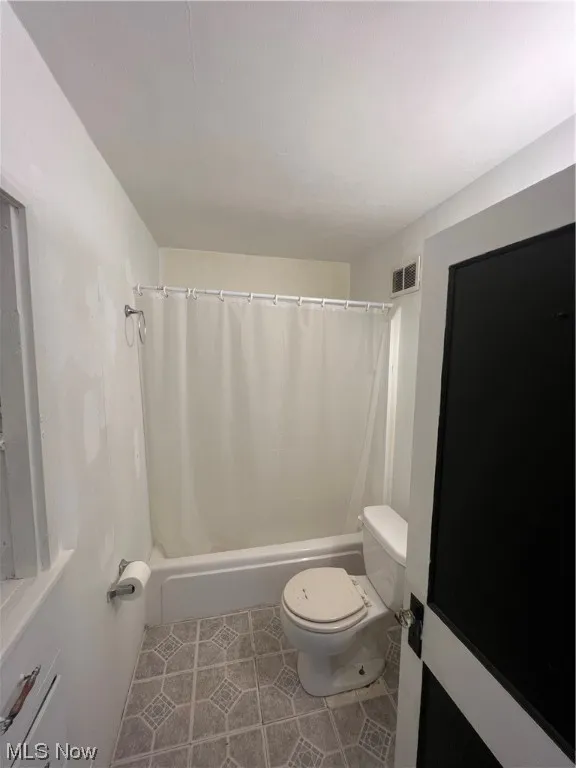 Bathroom featuring toilet, shower / tub combo, and tile floors