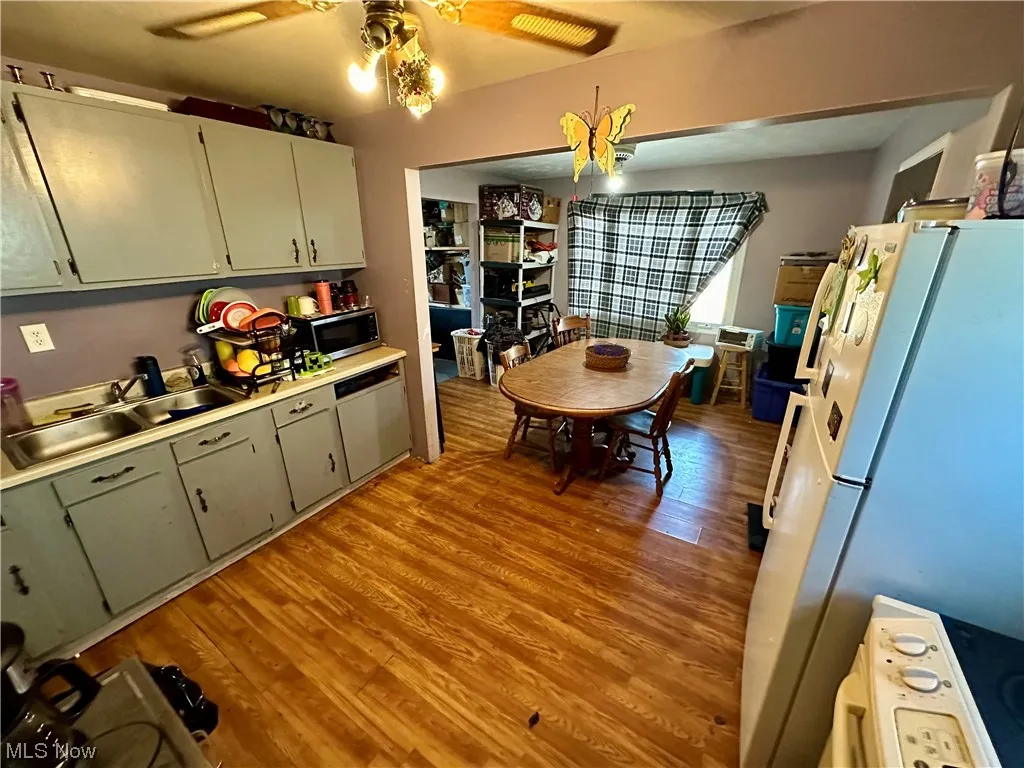Kitchen featuring green cabinets, sink, white appliances, ceiling fan, and light wood-type flooring