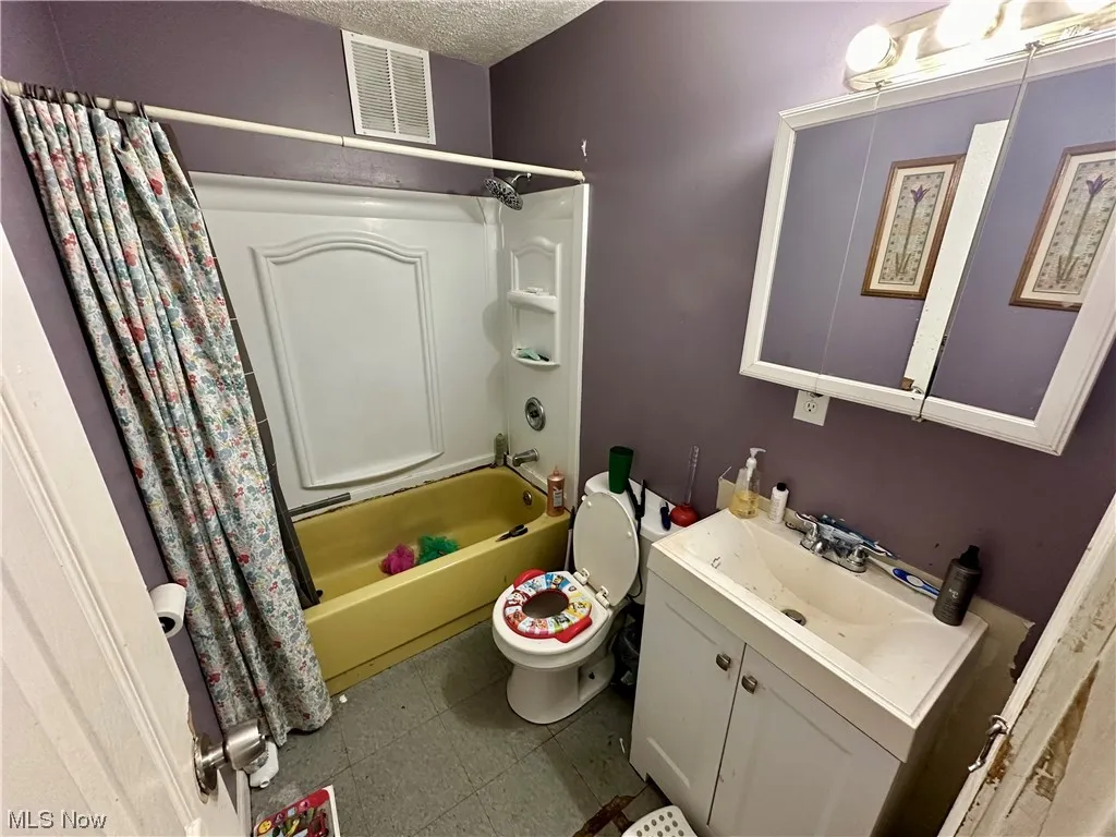 Full bathroom with vanity, shower / bath combination with curtain, toilet, a textured ceiling, and tile floors
