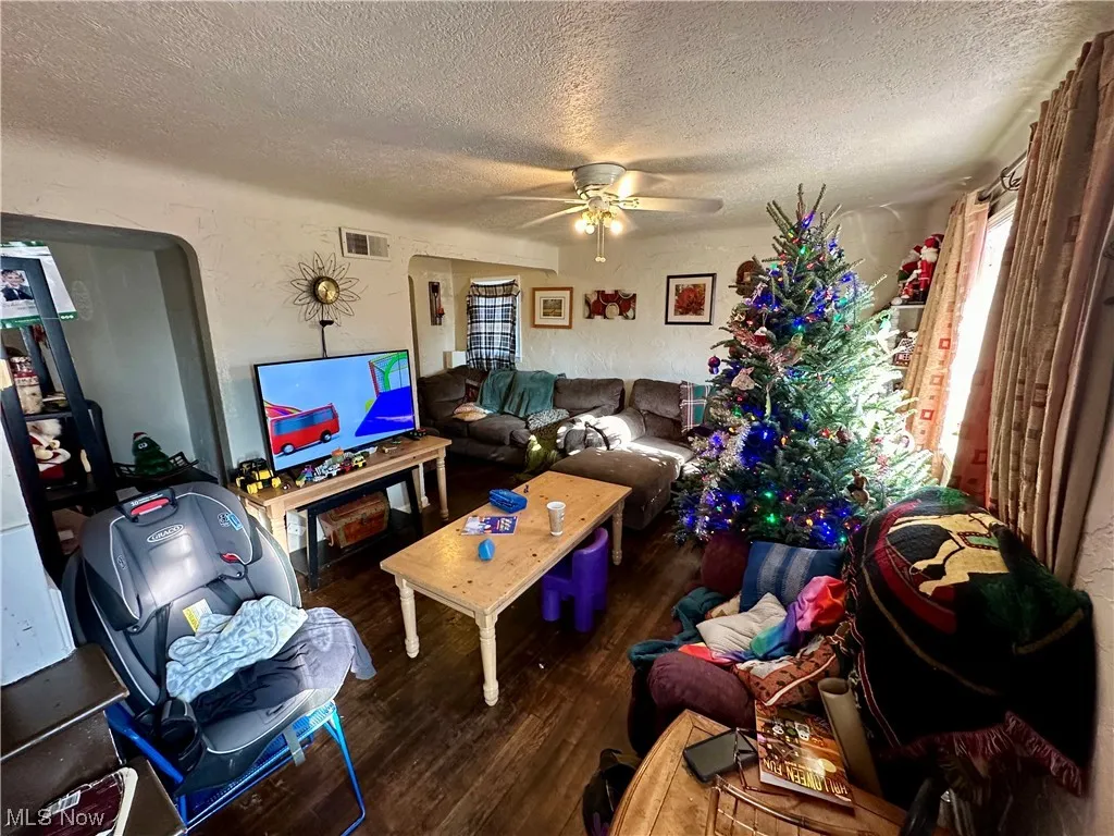 Living room with dark wood-type flooring, ceiling fan, and a textured ceiling