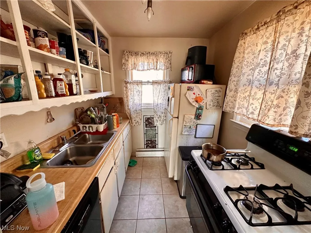 Kitchen featuring light tile flooring, white refrigerator, sink, and range with gas cooktop
