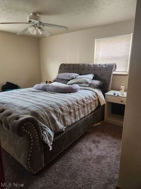 Carpeted bedroom with ceiling fan and a textured ceiling