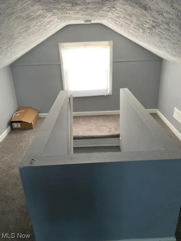 Stairway featuring dark carpet, vaulted ceiling, and a textured ceiling