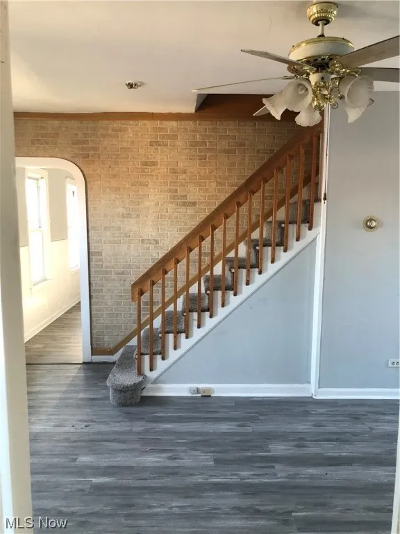 Staircase featuring dark wood-type flooring, ceiling fan, and brick wall