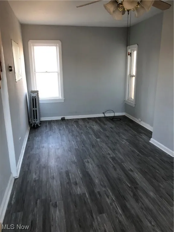 Unfurnished room featuring dark wood-type flooring, ceiling fan, and radiator heating unit