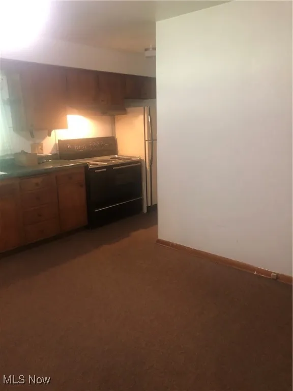 Kitchen featuring baseboards, range, dark countertops, refrigerator, and dark carpet