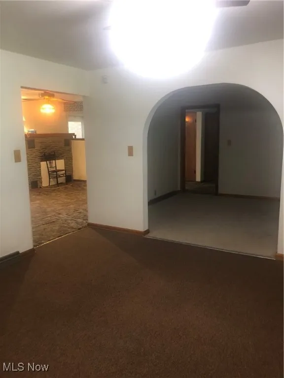 Carpeted empty room featuring baseboards, arched walkways, and a stone fireplace