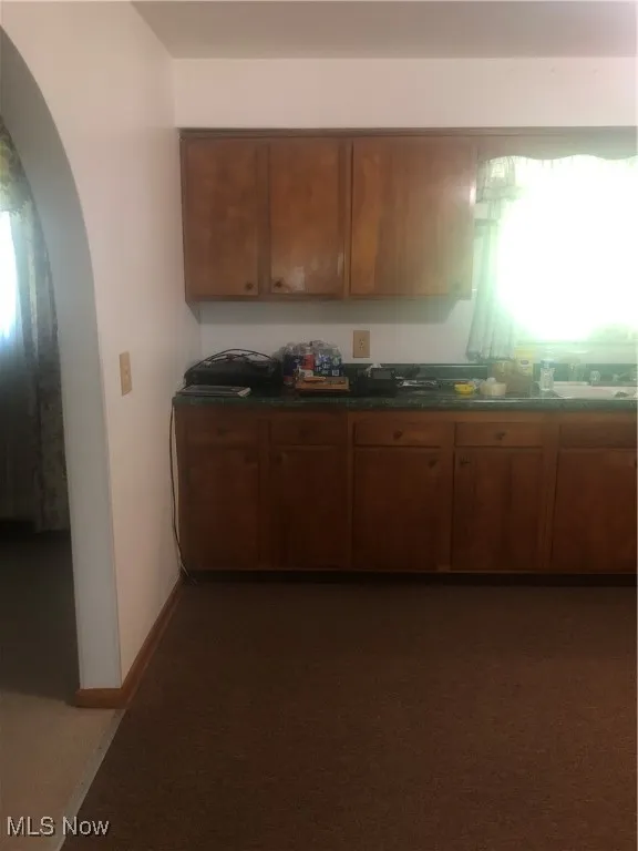 Kitchen featuring dark countertops, brown cabinets, arched walkways, and baseboards