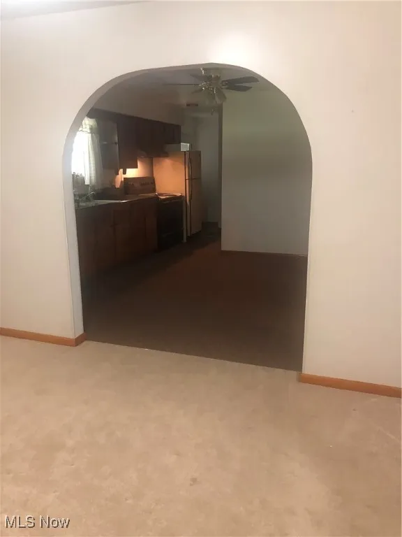 Hallway featuring baseboards, dark carpet, and arched walkways