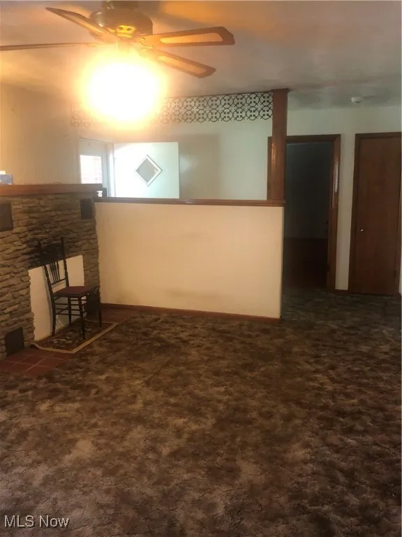 Empty room featuring ceiling fan, a stone fireplace, and carpet
