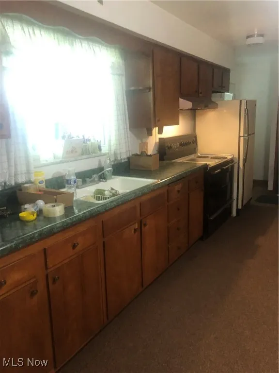 Kitchen featuring dark countertops, stove, brown cabinets, ventilation hood, and a sink
