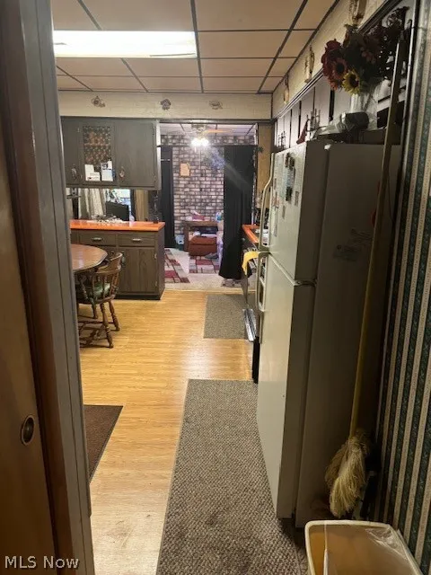 Kitchen with a drop ceiling, refrigerator, light hardwood / wood-style flooring, and brick wall
