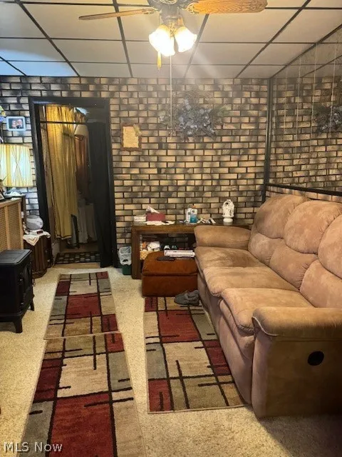 Living room with a drop ceiling, carpet, brick wall, and ceiling fan