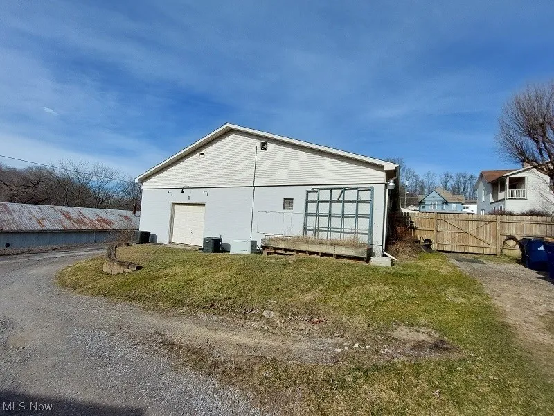 View of side of property featuring central air condition unit, a lawn, and a garage