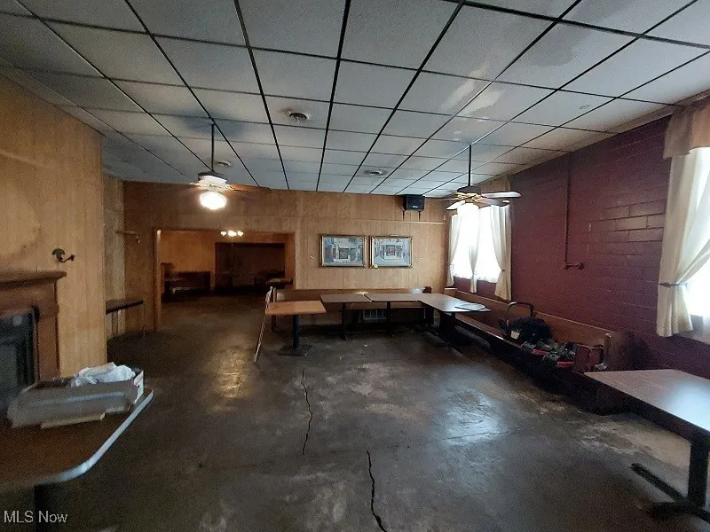 Misc room with a drop ceiling, wood walls, and ceiling fan