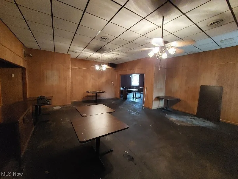 Basement featuring a paneled ceiling, ceiling fan, and wooden walls