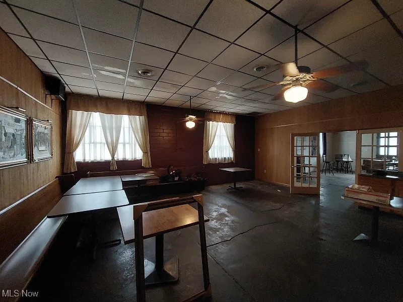 Dining area featuring a paneled ceiling, ceiling fan, and wood walls