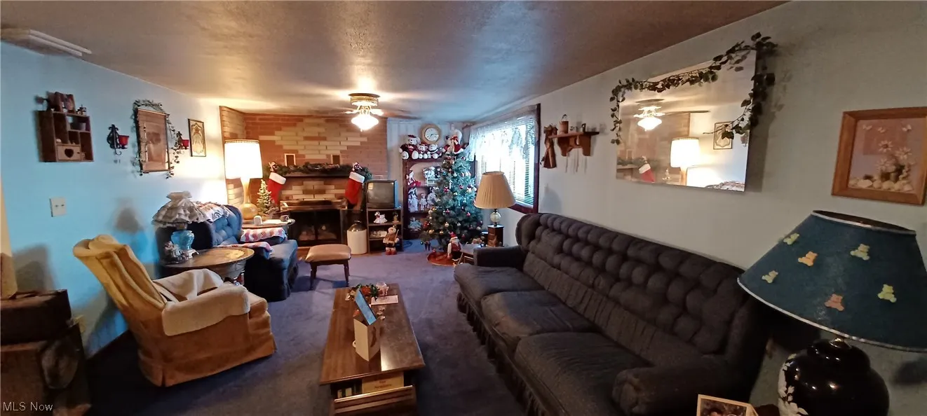 Carpeted lower level living room featuring brick wall, ceiling fan, and a brick fireplace