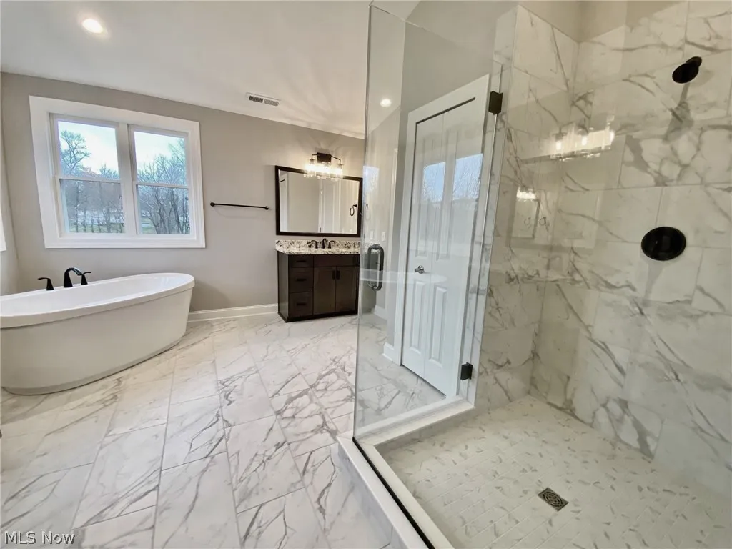 Bathroom with separate vanities, large tile shower shower, stand alone tub, and tile floors