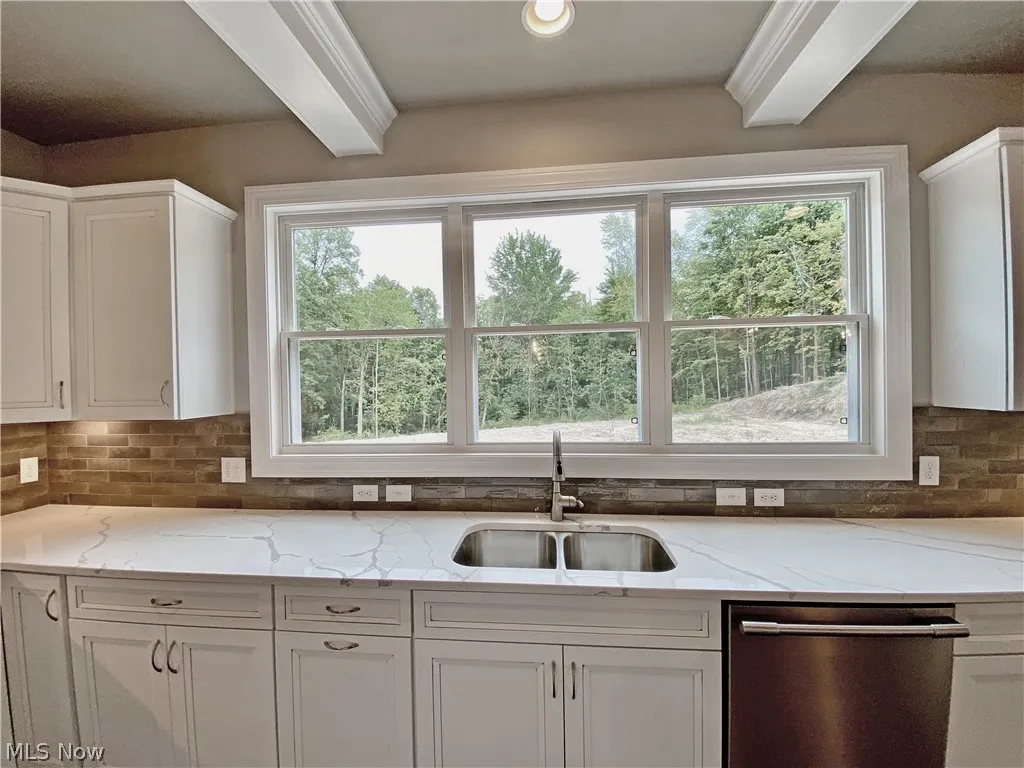 Kitchen with plenty of natural light, stainless steel dishwasher, light  quartz counters, white cabinetry, and sink