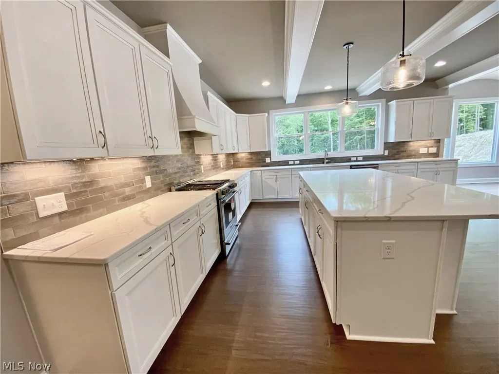 Kitchen featuring stainless steel range, white cabinets, decorative light fixtures, dark hardwood flooring, and a kitchen island
