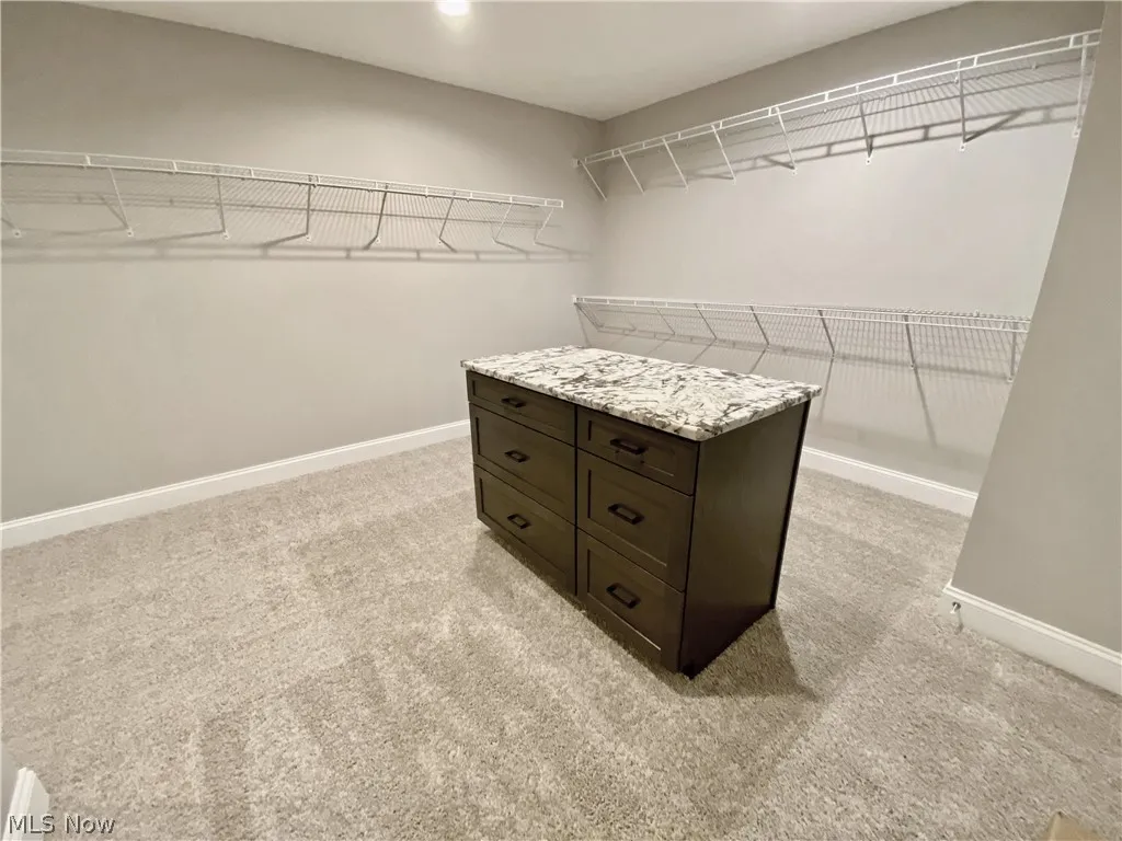Master walk in closet with center island and light colored carpet