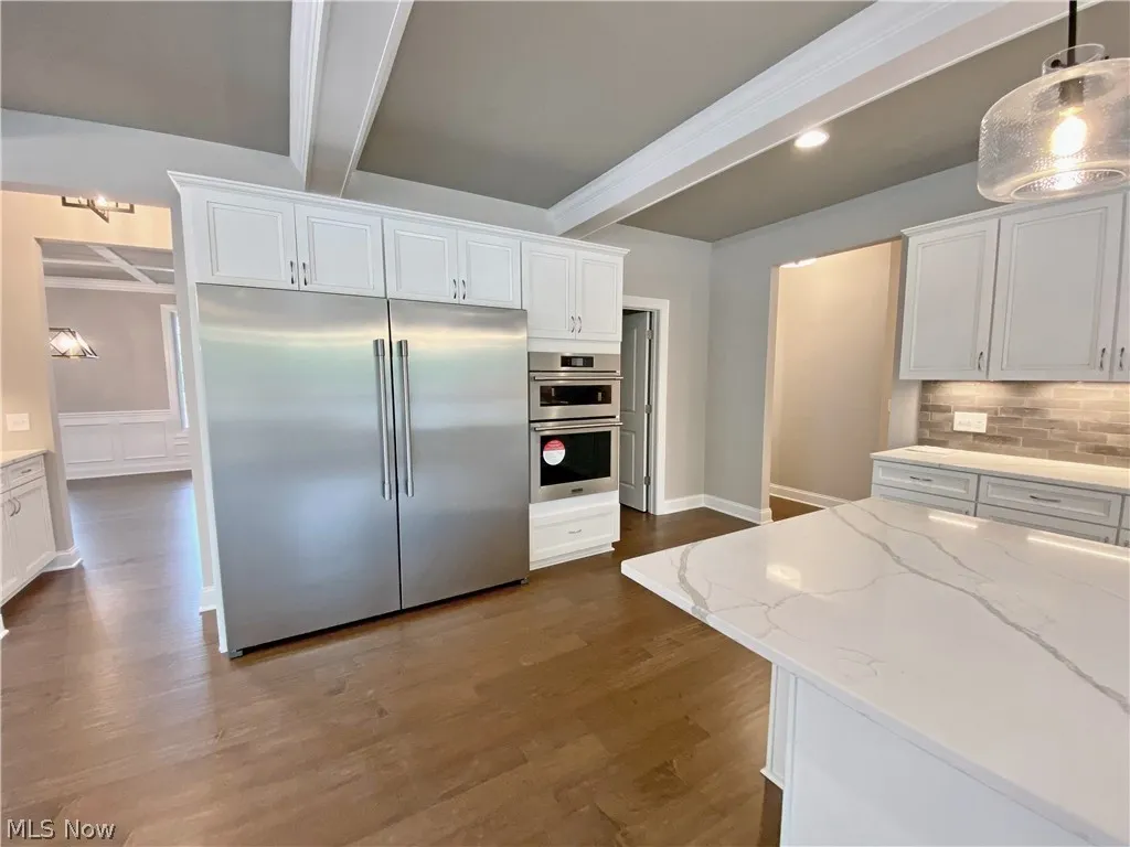 Kitchen featuring hanging light fixtures, beamed ceiling, wood-type flooring, white cabinets, and stainless steel appliances