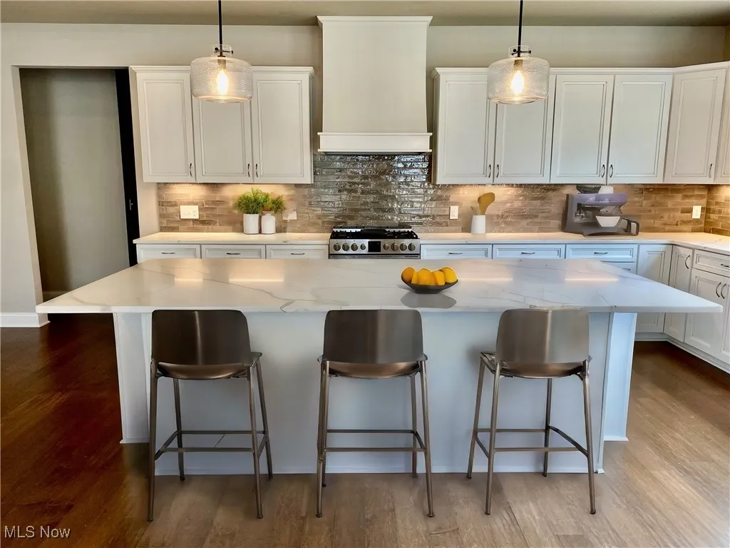Kitchen with white cabinets, pendant lighting, a center island, and custom range hood