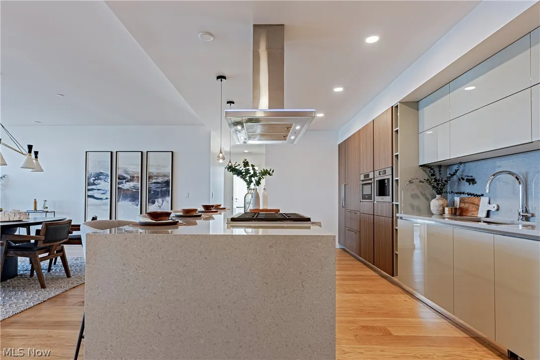 Kitchen featuring decorative light fixtures, a kitchen island, island range hood, light wood-type flooring, and sink
