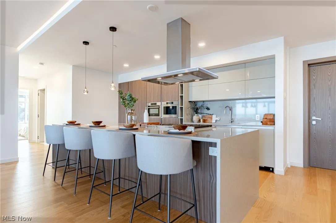 Kitchen featuring oven, tasteful backsplash, island exhaust hood, and light hardwood / wood-style flooring