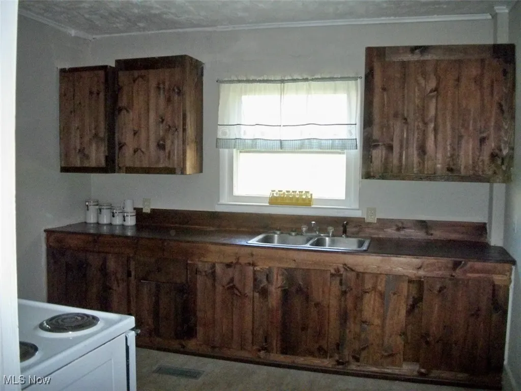Kitchen with white range with electric stovetop, dark countertops, crown molding, and a sink