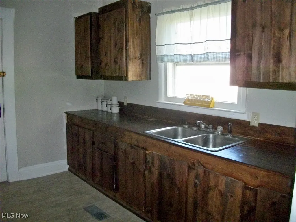 Kitchen featuring dark countertops, a sink, baseboards, and visible vents