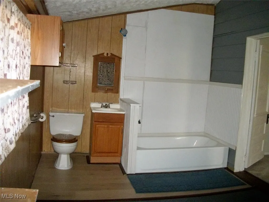Full bathroom with wood finished floors, toilet, a washtub, and vanity