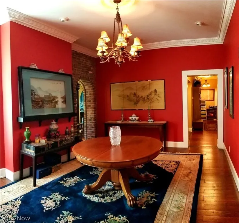 Dining area featuring dark hardwood / wood-style floors, ornamental molding, brick wall, and an inviting chandelier