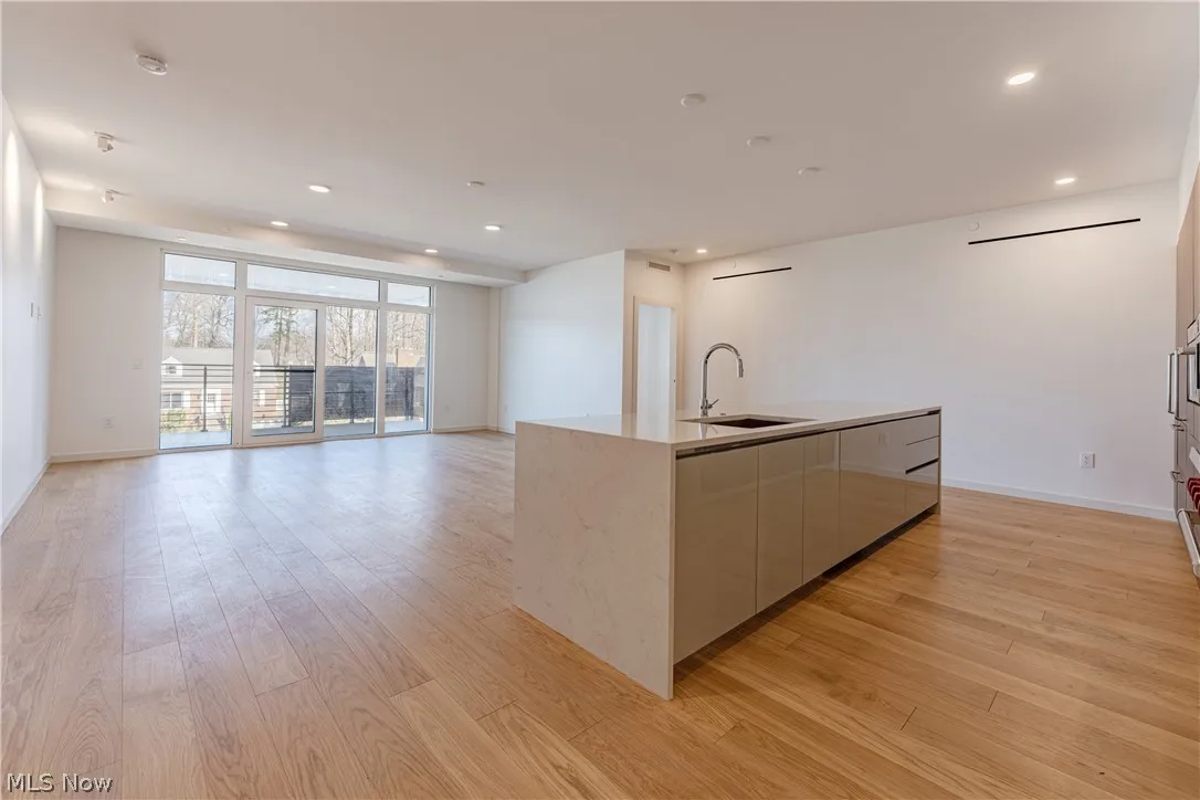 Kitchen with wall oven, a center island with sink, light hardwood / wood-style floors, and sink