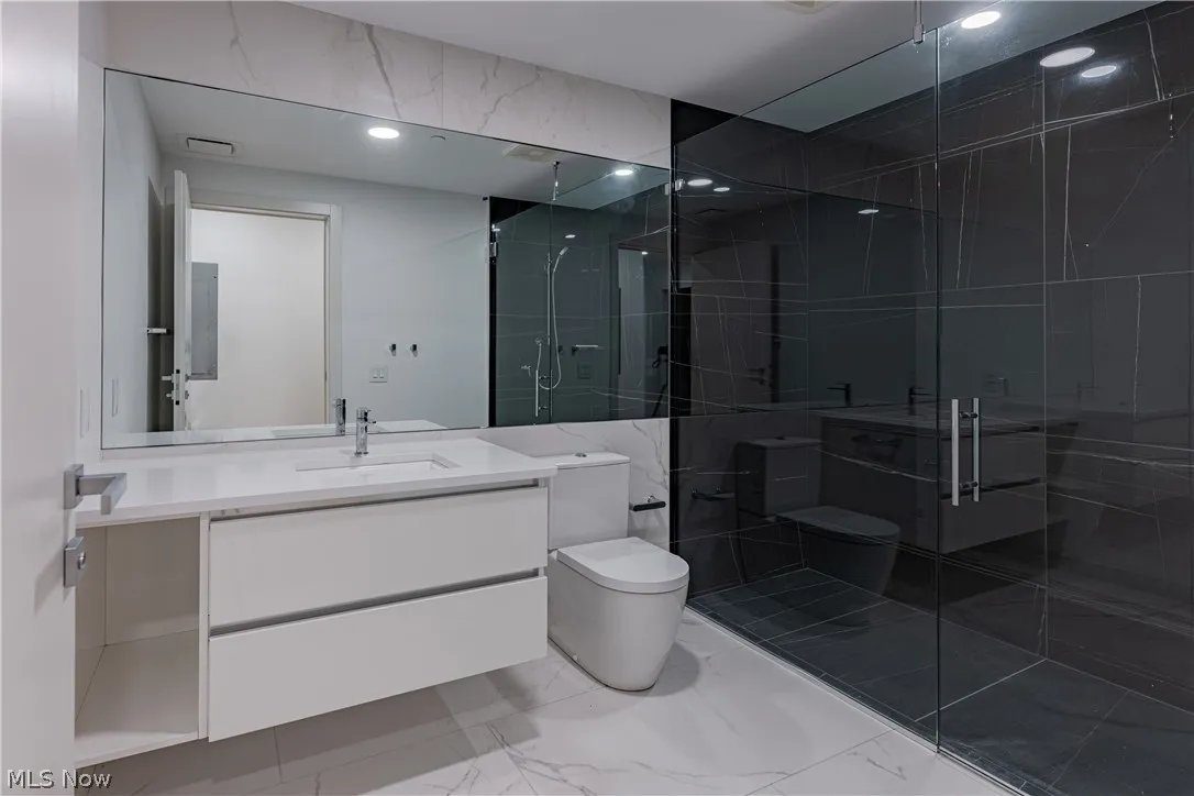 Bathroom with an enclosed shower, vanity, tile floors, and toilet