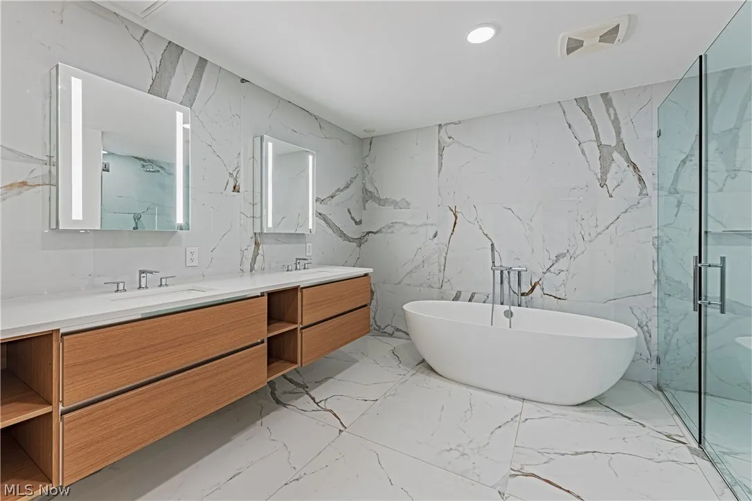 Bathroom featuring tile walls, independent shower and bath, tile floors, and double vanity