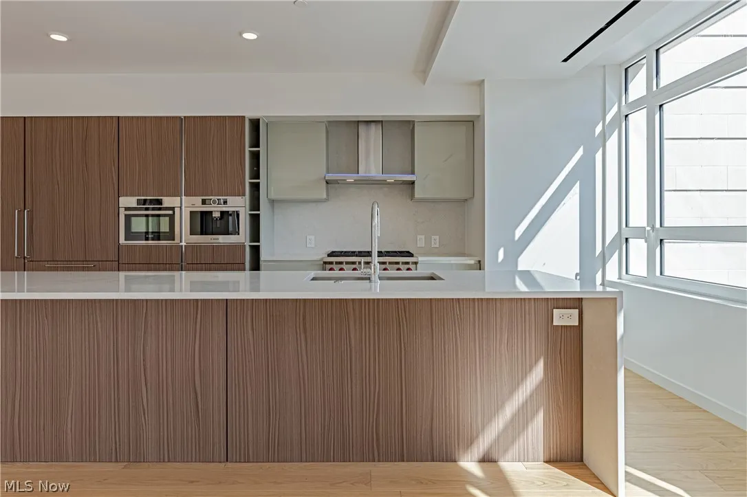 Kitchen featuring wall chimney exhaust hood, light hardwood / wood-style flooring, oven, and backsplash
