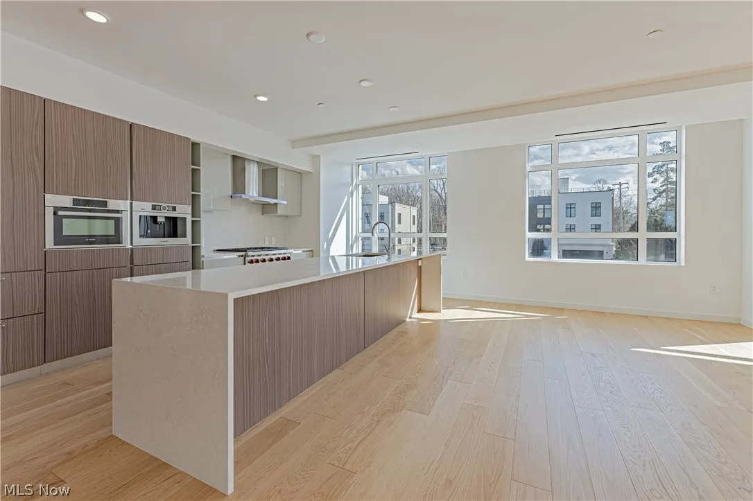 Kitchen featuring oven, wall chimney range hood, a center island with sink, and light wood-type flooring
