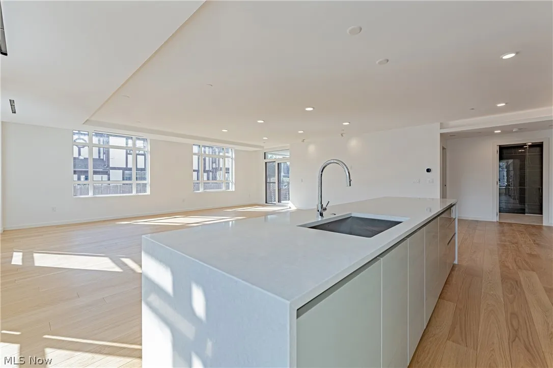 Kitchen with sink, a center island with sink, light hardwood / wood-style floors, and white cabinetry