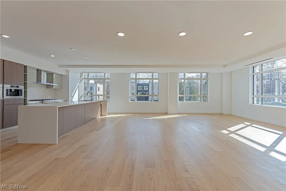 Kitchen featuring wall chimney exhaust hood, an island with sink, light wood-type flooring, and a wealth of natural light