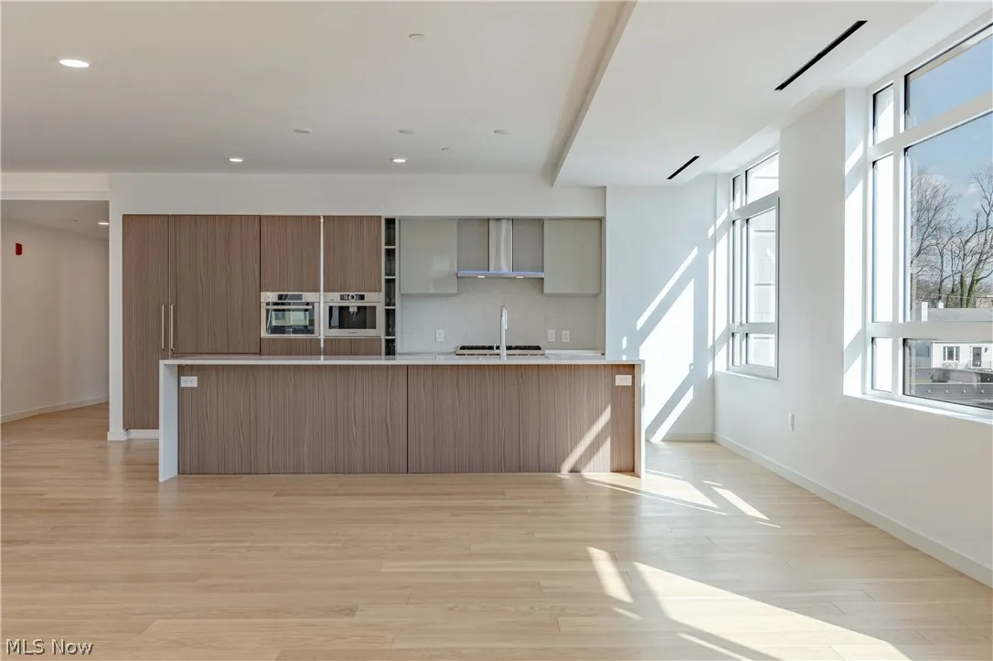 Kitchen featuring plenty of natural light, wall chimney exhaust hood, and a kitchen island with sink